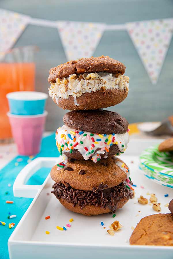 Stack of three Easy Ice Cream Sandwiches on a white tray on a teal placemat with bright cups and punch and a party banner in the background