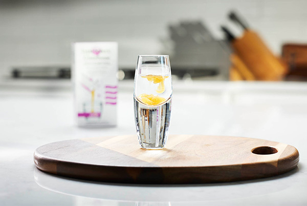 LivOn Labs Glutathione liposomal supplement in a shot glass of water on a wood cutting board in a modern white kitchen