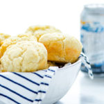 White bowl with white and royal blue stripped napkin with Beer Bread Muffins inside and a can of gluten-free beer in the background