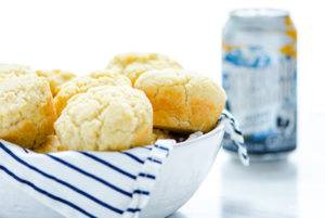 White bowl with white and royal blue stripped napkin with Beer Bread Muffins inside and a can of gluten-free beer in the background