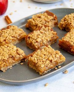 Caramel Apple Bars on a gray rectangular serving platter with apple slices on the sides for garnish and oats and red apple in the background