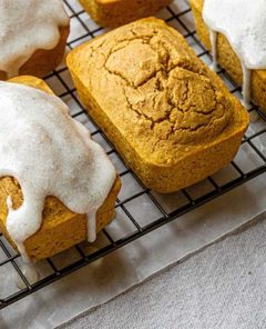 Overhead view of Chai-Spiced Mini Pumpkin Loaves on a black wire cooling rack set over parchment paper on an off-white tablecloth