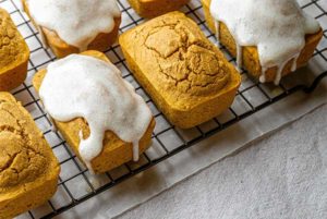 Overhead view of Chai-Spiced Mini Pumpkin Loaves on a black wire cooling rack set over parchment paper on an off-white tablecloth