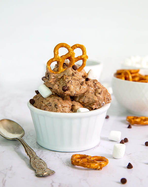 Closeup of Not-So-Rocky Road Ice Cream in a white ramekin topped with pretzels with a vintage silver spoon next to it on a white marble counter