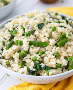 Closeup of Pea and Asparagus Risotto in a white bowl with mustard yellow napkin underneath on a white table