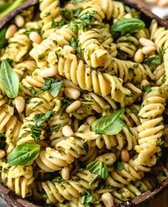Closeup of Pesto Pasta topped with fresh basil and pine nuts in a wooden bowl on a wooden table