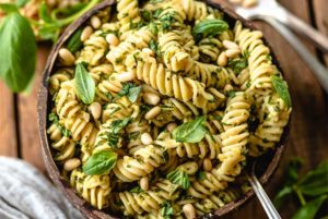 Closeup of Pesto Pasta topped with fresh basil and pine nuts in a wooden bowl on a wooden table