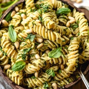 Closeup of Pesto Pasta topped with fresh basil and pine nuts in a wooden bowl on a wooden table