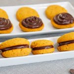 Closeup of Pumpkin Whoopie Pies in white dishes with some fully assembled and others open-faced to show the chocolate filling