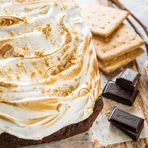 Closeup of S'more Brownie Bread on a wooden board with graham crackers and chocolate squares and roasted marshmallows on sticks next to the bread