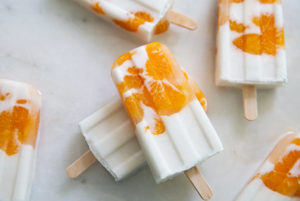 Overhead view of white and orange Sunshine Popsicles on a white marble countertop