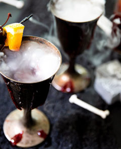 Vampire Sangria in antique pewter wine glasses with dry ice smoke coming off them and garnished with a dark cherry and orange slice