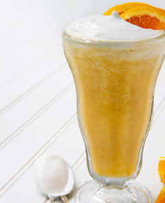 Vitamin C Smoothie in a tall glass with whipped coconut cream on top and orange slice garnish on a white background