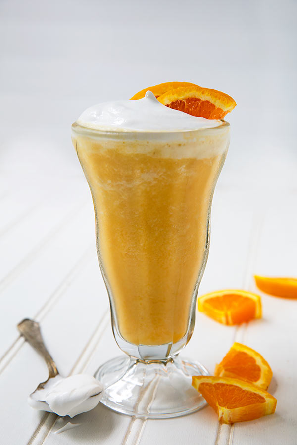 Vitamin C Smoothie in a tall glass with whipped coconut cream on top and orange slice garnish on a white background
