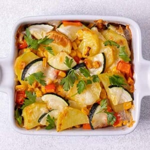 Closeup overhead view of Zucchini Chicken and Potato Casserole in a white ceramic square baking dish on a white table