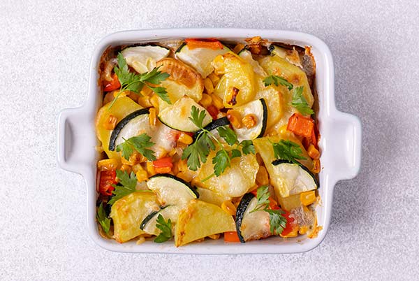 Closeup overhead view of Zucchini Chicken and Potato Casserole in a white ceramic square baking dish on a white table