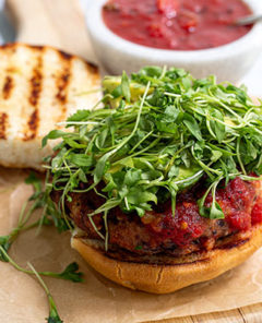 Black Bean Salsa Burger with the bun open with grill marks on it and the patty topped with microgreens on a wooden cutting board lined with beige parchment paper