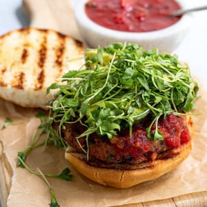 Black Bean Salsa Burger with the bun open with grill marks on it and the patty topped with microgreens on a wooden cutting board lined with beige parchment paper