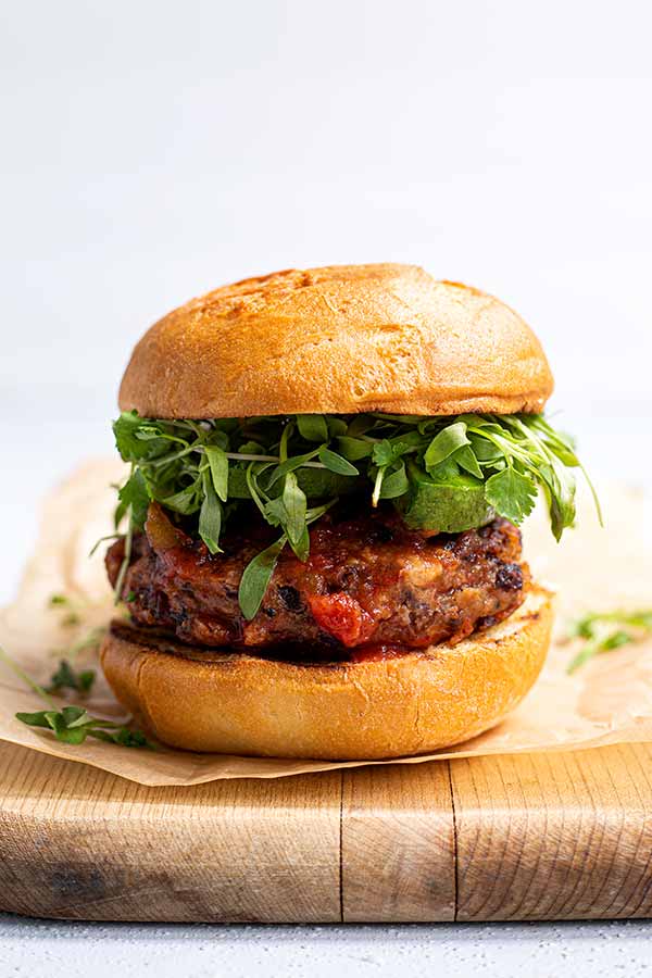 Closeup of Black Bean Salsa Burger on a piece of beige parchment paper on top of a thick wooden cutting board in front of a white background