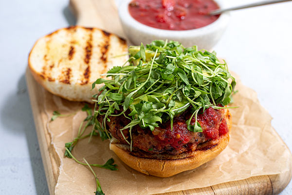 Black Bean Salsa Burger with the bun open with grill marks on it and the patty topped with microgreens on a wooden cutting board lined with beige parchment paper