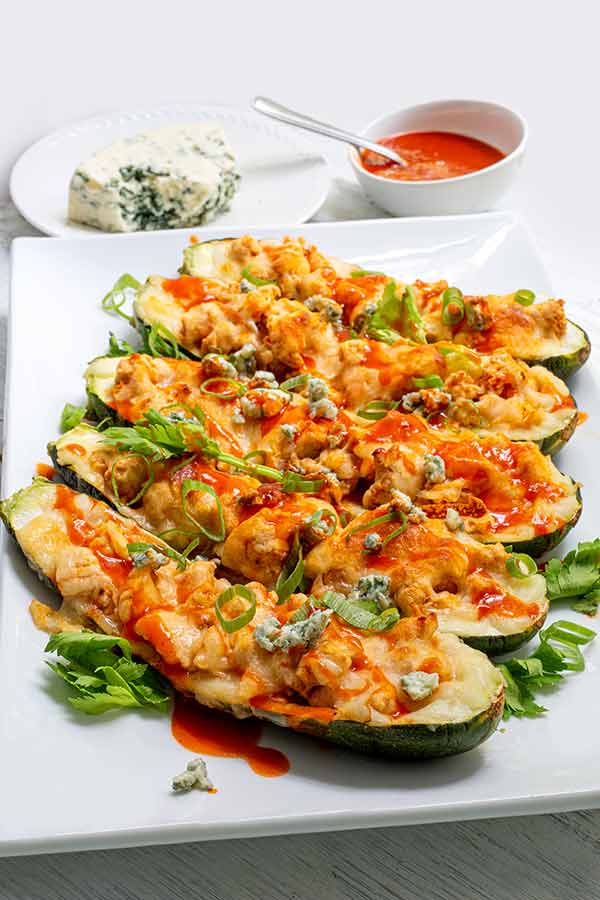 Buffalo Chicken Zucchini Boats in a row on a white rectangular platter on a white background