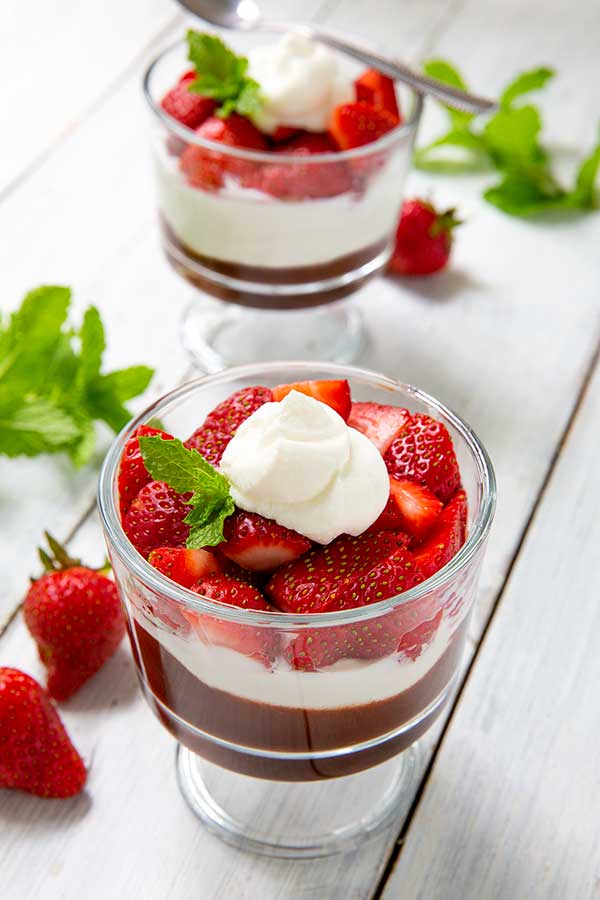 Chocolate Strawberry Parfaits topped with fresh mint leaves on a white wood table with strawberries and mint leaves scattered around