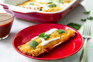 Lazy Enchiladas on a bright red plate with a red and white baking dish with enchiladas inside in the background