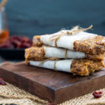 No-Bake Granola Bars wrapped with parchment paper and twine stacked on top of each other on a dark wood cutting board against a dark gray background
