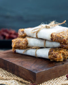 No-Bake Granola Bars wrapped with parchment paper and twine stacked on top of each other on a dark wood cutting board against a dark gray background