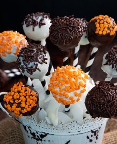 Carrot Cake Pops decorated in orange and brown sprinkles and place in a white decorative bucket with burlap ribbon against a black background