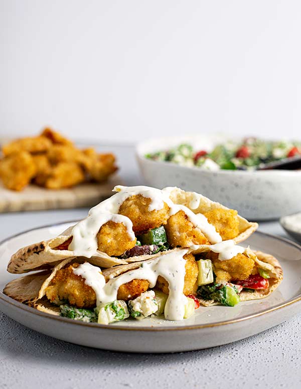 Chicken Tender Pitas stacked on a white plate with tzatziki sauce drizzled on top against a white background