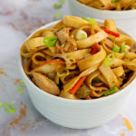 Closeup of Gluten-Free Chow Mein in a white bowl topped with green onions on a white marble counter