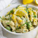 Closeup of Lemon Ricotta Pesto Pasta in a white bowl with fresh lemon slices in the background on a white table