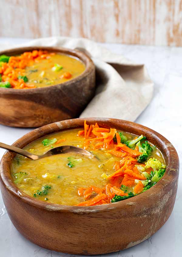 Plant-Based Broccoli 'Cheese' Soup in a brown bowl on a white table with another bowl of soup in the background