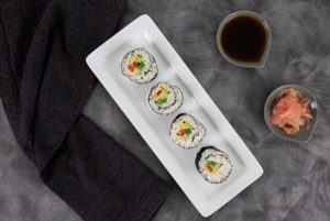 Overhead view of Vegetarian Sushi on a white rectangular plate with a black cloth napkin on a dark gray table