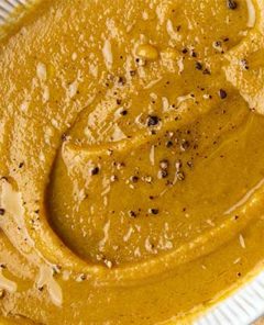 Close-up view of Acorn Squash Soup in a white oval bowl with fresh cracked pepper on top