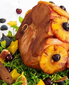 Close-up of Angela's Ham dotted with pineapple and cherries on a bed of greens with figs and cherries surrounding the ham