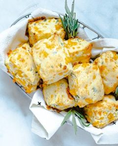 Cheddar Sage Biscuits in a silver wire basket lined with a cloth white napkin and fresh sage garnish