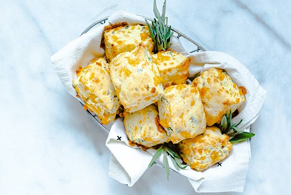 Cheddar Sage Biscuits in a silver wire basket lined with a cloth white napkin and fresh sage garnish