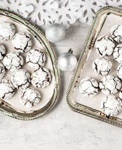 Overhead view of Chocolate Amaretti on two silver platters with silver ball ornaments and cut-out snowflakes on a white table
