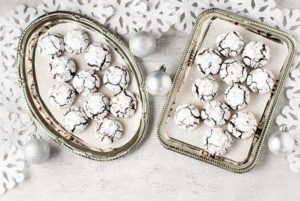 Overhead view of Chocolate Amaretti on two silver platters with silver ball ornaments and cut-out snowflakes on a white table