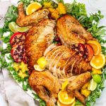 Overhead view of Citrus and Herb Turkey on a white oval platter garnished with fresh herbs and sliced pomegranates and oranges