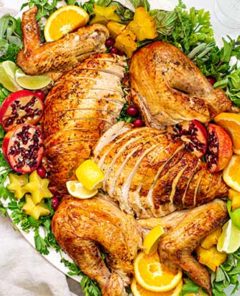 Overhead view of Citrus and Herb Turkey on a white oval platter garnished with fresh herbs and sliced pomegranates and oranges