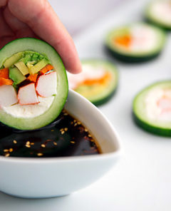Closeup of a hand dipping Cucumber Sushi into soy sauce in a white ramekin
