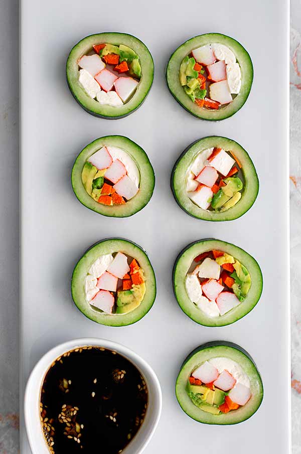 Overhead view of Cucumber Sushi in two columns on a white rectangular serving dish with a ramekin of soy sauce
