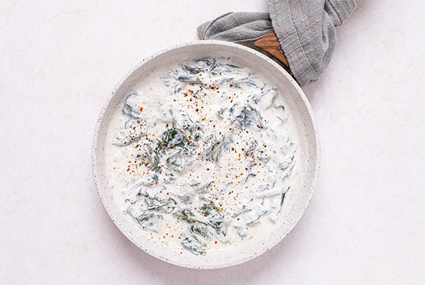 Overhead view of Easy Creamy Spinach in a white ceramic skillet with wooden handle and gray towel wrapped around the handle