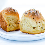 Two Everything Bagel Dinner Rolls on a stack of two small white plates against a white background