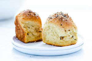 Two Everything Bagel Dinner Rolls on a stack of two small white plates against a white background