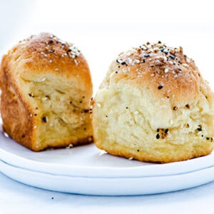 Two Everything Bagel Dinner Rolls on a stack of two small white plates against a white background