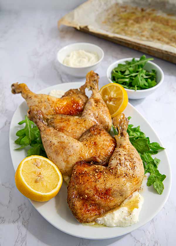 Garlic-Lemon Chicken Legs on a white oval platter garnished with arugula and lemon on a white marble countertop